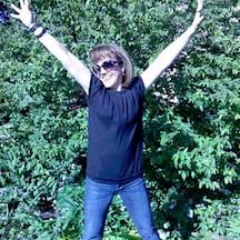 Hillary posing with arms outstretched in front of a bush