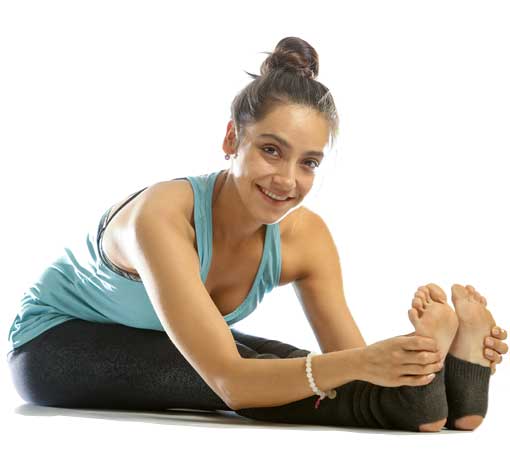 Woman seated, easily reaching for her toes while smiling at the camera