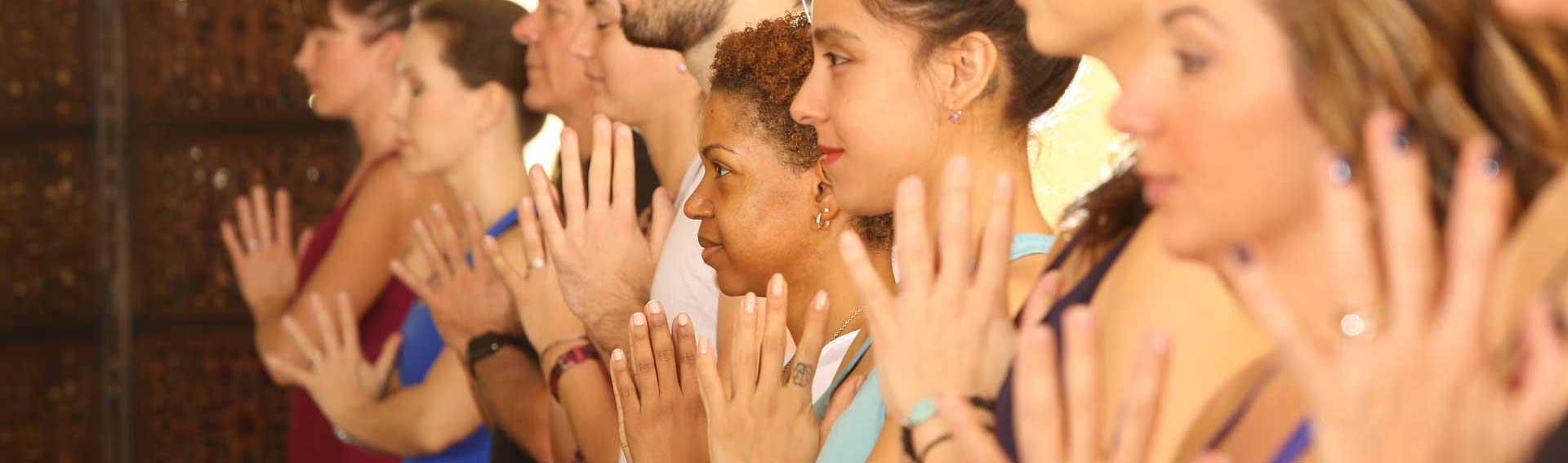 Yoga class standing in a row with hands clasped in front of them